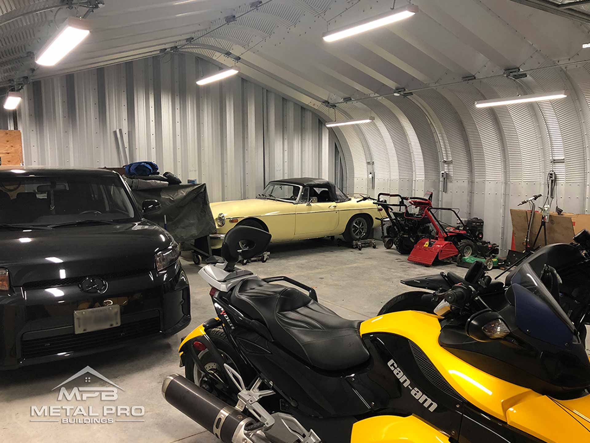 interior of a quonset garage building with two vehicles and a motorcycle parked