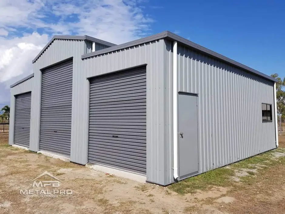 Large gray metal garage with three roll-up doors and a side entry, by Metal Pro Buildings.