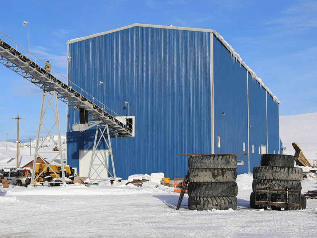 Large blue steel industrial building in snowy area with conveyor system and stacked tires.