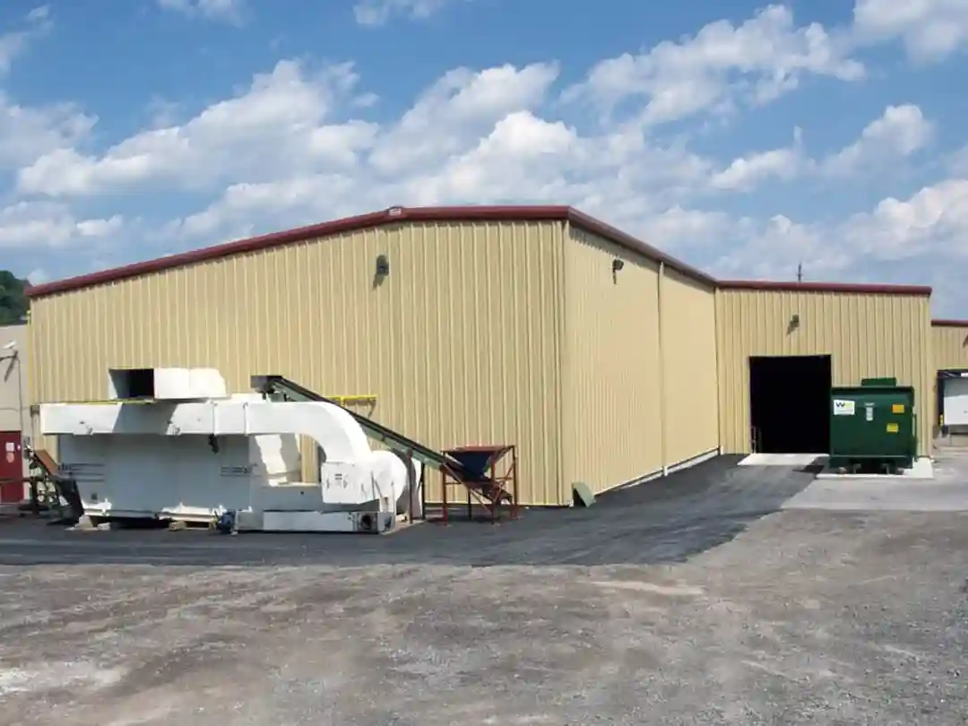 Large tan industrial steel building with red trim, equipment outside, and clear blue sky.