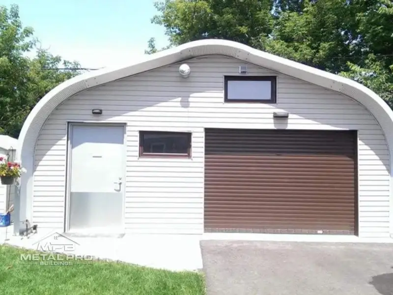 Quonset-style metal garage with curved roof, brown roll-up door, and side entry by MPB.