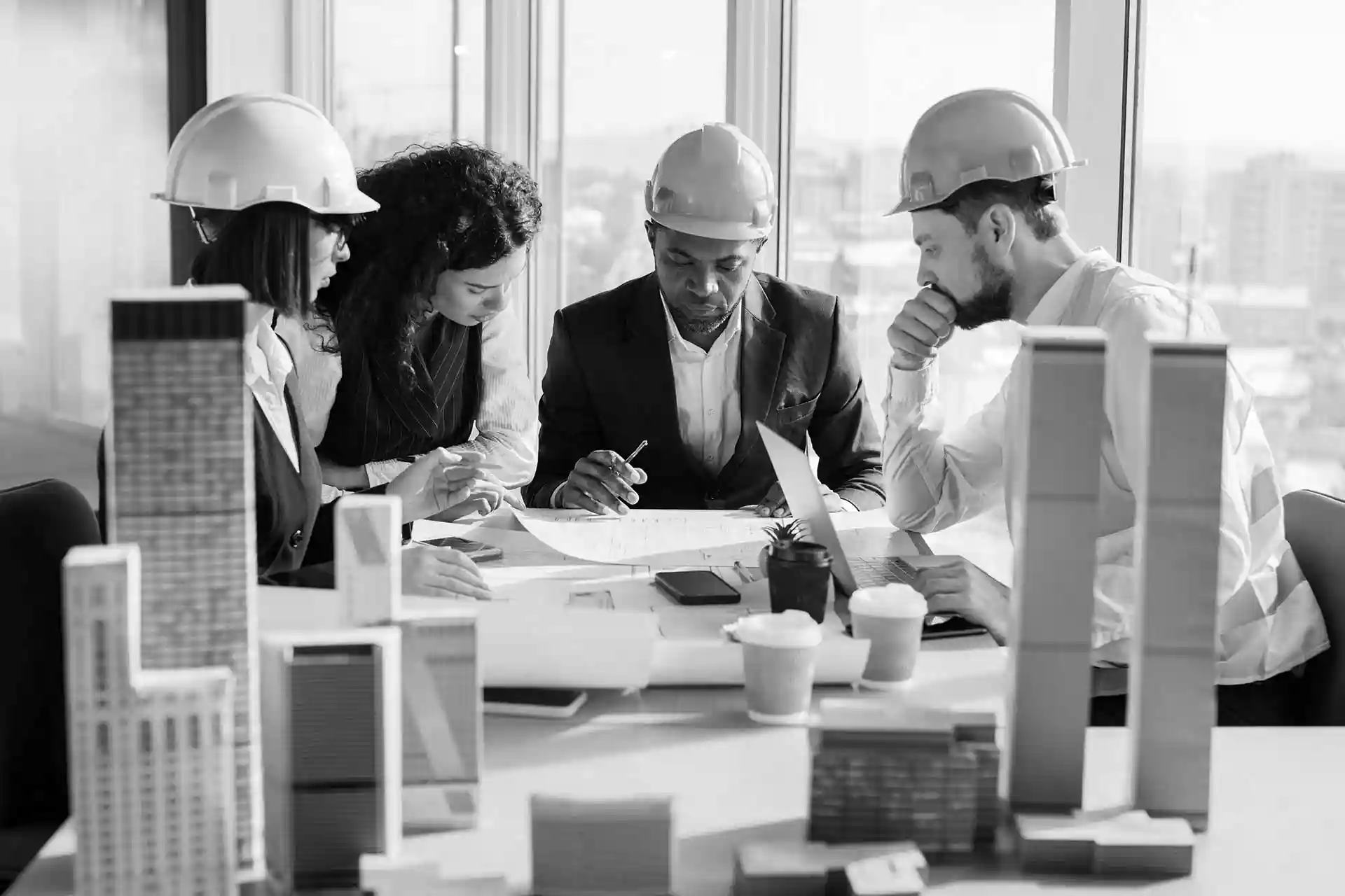 Architects in hard hats reviewing blueprints around a table with scale models.